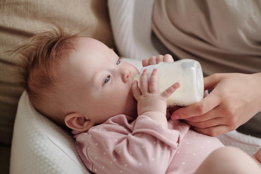 beba devojčica pije mleko dok drži flašicu