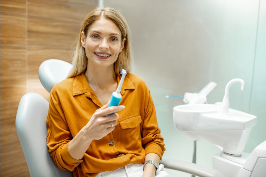nasmejana zena drzi elektricnu cetkicu u stomatoloskoj ordinaciji