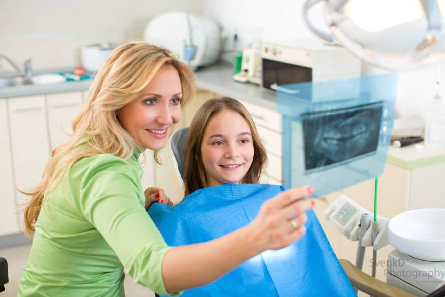 stomatolog pokazuje devojčici snimak njenih zuba pre nego što usledi vađenje mlečnih zuba